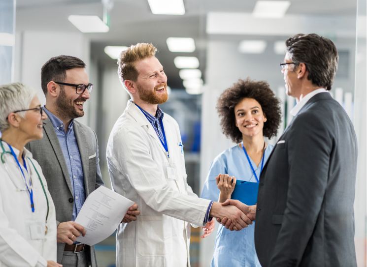 Photo of physican team and doctor meeting with a client who is wearing a blazer. Doctor is shaking client's hand